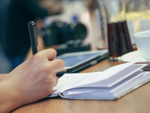 Persoon die aantekeningen maakt in een notitieboekje aan een cafétafel, nadenken over loopbaan en richting