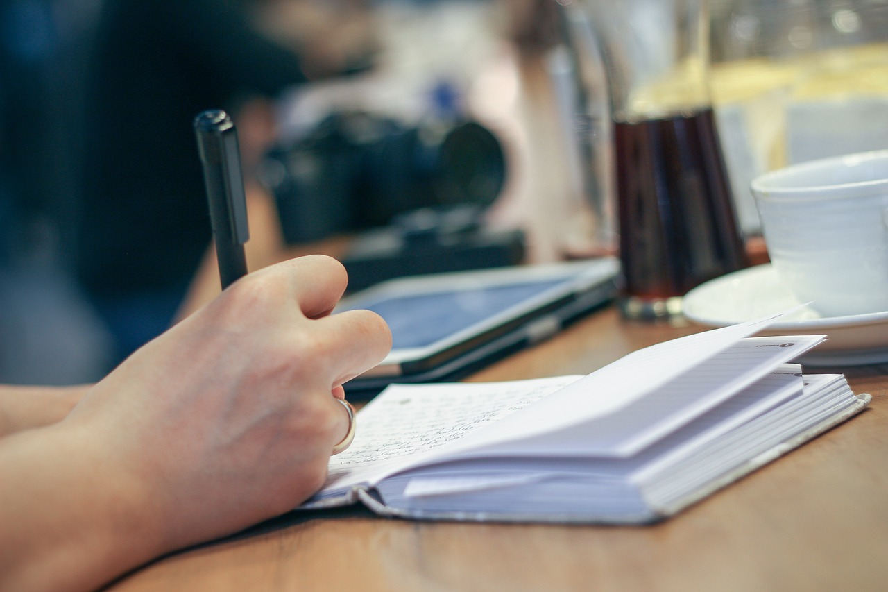 Persoon die aantekeningen maakt in een notitieboekje aan een cafétafel, nadenken over loopbaan en richting